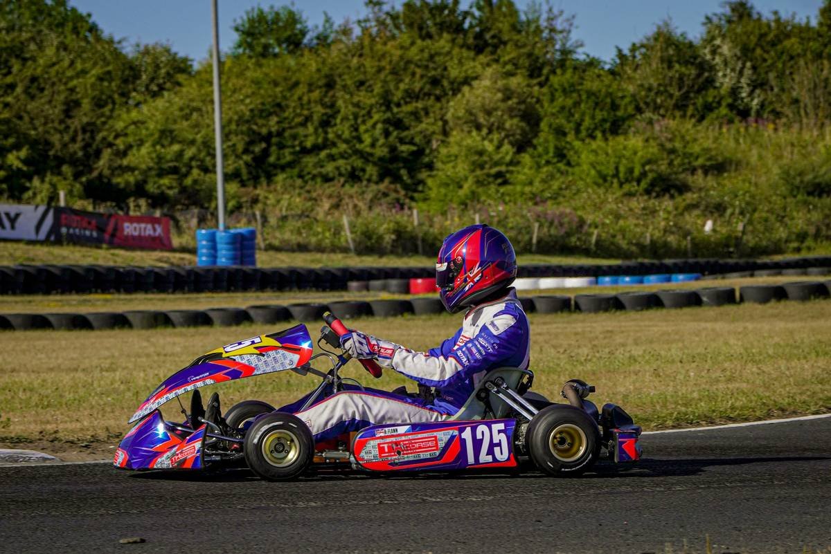 Young MotoGP rider posing next to a mini motorcycle in a garage workshop.